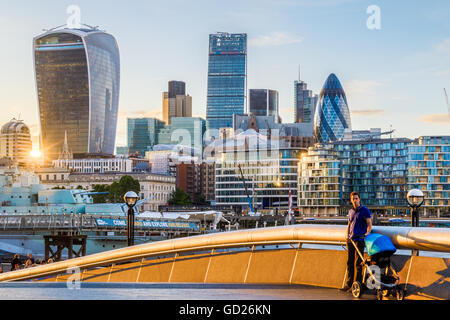 London, Regno Unito - 24 Giugno 2016 - un giovane padre con un bambino la PRAM contro uno sfondo di nel distretto finanziario londinese al tramonto Foto Stock