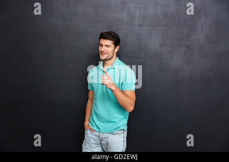 Bel giovane uomo sorridente puntando alla fotocamera su sfondo nero Foto Stock