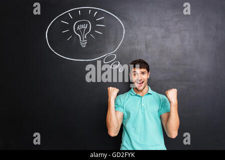 Successo allegro giovane uomo avente un'idea e celebrare il successo su su sfondo blackboard Foto Stock