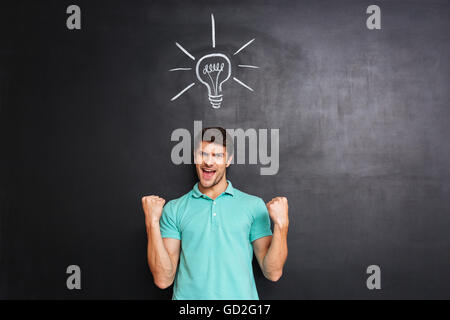 Felice fiducioso giovane per celebrare il successo e avente un'idea su sfondo blackboard Foto Stock