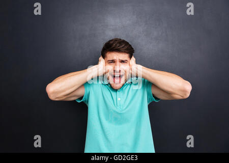 Uomo informale che coprono le orecchie e le grida isolate su lavagna Foto Stock