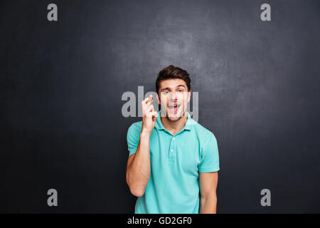 Bel giovane con il suo dito attraversato isolato sulla lavagna, fortuna gesto Foto Stock