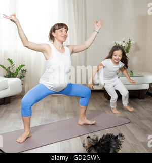 Famiglia uno stile di vita sano concetto. Gravidanza Yoga e fitness. Giovani felici yoga in gravidanza mamma lavora fuori in living room interior Foto Stock