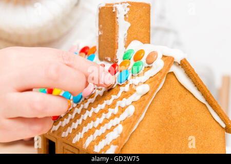 Le mani delle donne sono fissati al tetto del colorato di confetti di gingerbread house Foto Stock