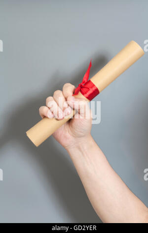 Diploma con un nastro rosso in mano su sfondo grigio Foto Stock