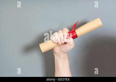 Diploma con un nastro rosso in mano su sfondo grigio Foto Stock