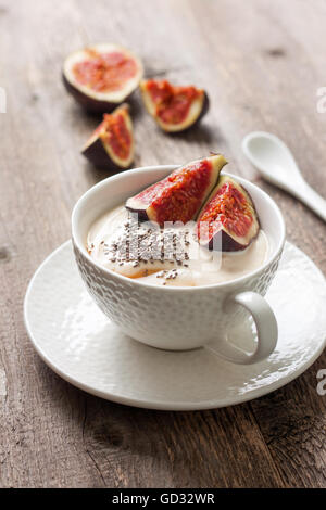 Yogurt con pezzi di fig, chia semi, il miele in un bicchiere di bianco su uno sfondo di legno Foto Stock