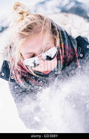 Una giovane donna in occhiali da sole soffiando la neve fresca dalle mani. Foto Stock