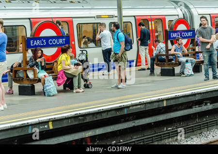 I passeggeri seduti sui banchi alla stazione della metropolitana di Earl's Court mentre si attende per il loro treno. Foto Stock