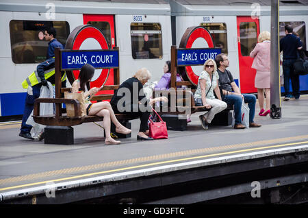 I passeggeri seduti sui banchi alla stazione della metropolitana di Earl's Court mentre si attende per il loro treno. Foto Stock