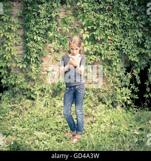 Carino young teen girl disegnare o scrivere i suoi pensieri in notebook nei pressi di antiche rovine coperte con wild grapevine. Immagine dai toni Foto Stock