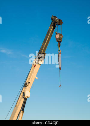 Dettaglio di un braccio telescopico di un camion gru montata con catene appese sul gancio, cielo blu in background Foto Stock