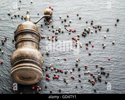 Grani di pepe colorato e il vecchio mulino di pepe su sfondo nero. Foto Stock