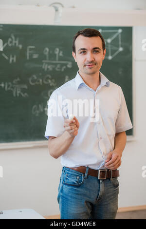 Bel giovane maschio di studente o insegnante rilassante permanente contro una lavagna verde Foto Stock