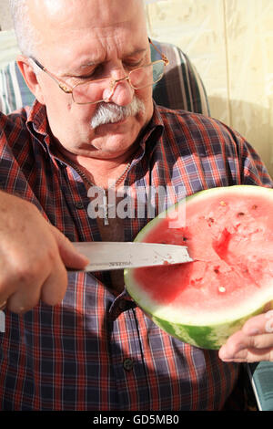 Uomo ucraino di alcuni 55-60 è il taglio di un water melon con un coltellino, godendo ucraino ricca di frutta e verdura harvest Foto Stock