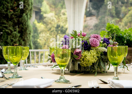 Tabella formale impostazione per un matrimonio con centrotavola floreali e colorati occhiali verdi davanti a una finestra di visualizzazione ampia overlookin Foto Stock