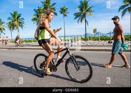 RIO DE JANEIRO - Marzo 6, 2016: donna brasiliana corse in bicicletta a fianco di pedoni sulla spiaggia di Ipanema beachfront road. Foto Stock