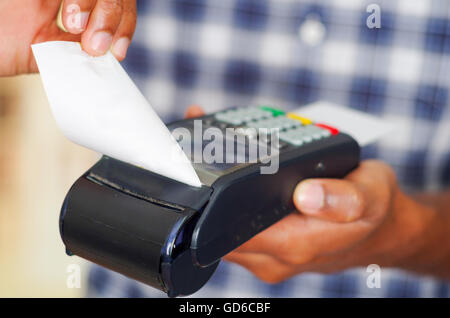 Uomo che indossa blu bianco disegno quadrato shirt elaborazione del pagamento con carta di credito terminale nella parte anteriore della fotocamera, closeup angolo Foto Stock