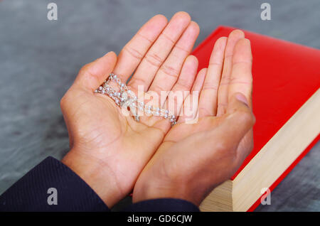 Rosso la bibbia giacente sulla scrivania blu con mans aprire le mani sopra prenota, rosario croce collocata all'interno, il concetto di religione Foto Stock