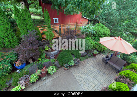 Giardino nel cortile paesaggistico con lastricatore mattoni patio hardscape alberi di piante in vaso arbusti stagno rocce mobili e granaio rosso Foto Stock