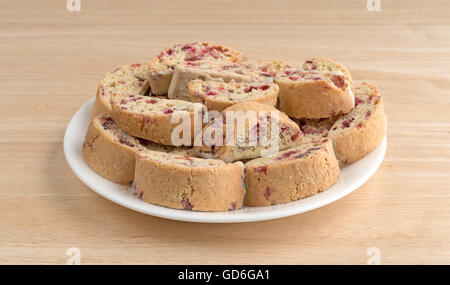 Vari biscotti con mirtilli e mandorle immersi nel cioccolato bianco su una piastra bianca in cima a una tavola di legno. Foto Stock