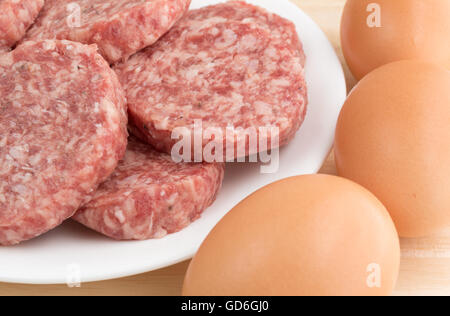 Vista ravvicinata di una piastra bianca con salsiccia polpette e uova a lato sulla cima di un contatore di legno alto. Foto Stock