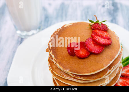 Vista dettagliata del pancake con fragole fresche e menta vicino al vetro con il latte sulla piastra bianca rosa su sfondo di legno. stack di pañca Foto Stock