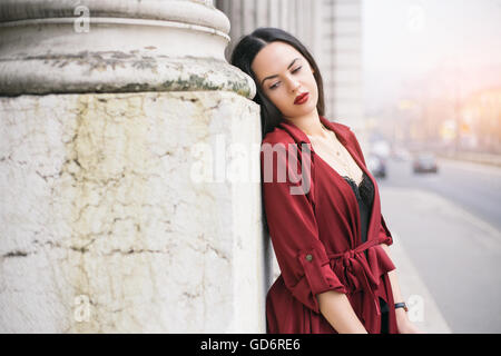 Ritratto di una donna in rosso cappotto appoggiata contro il muro Foto Stock