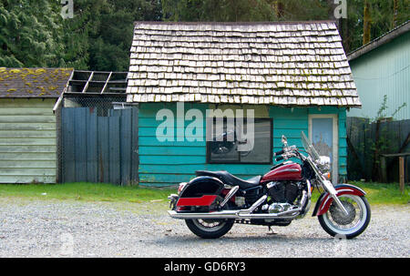 Un bel color mirtillo palustre di stile cruiser motociclo è parcheggiata di fronte a shingle con tetti color turchese cabina. Foto Stock