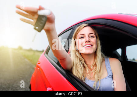 Donna attraente in una vettura che mostra i tasti al tramonto. Foto Stock