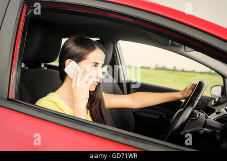 Bruna alla guida di una automobile rossa e parla a un telefono cellulare. Foto Stock