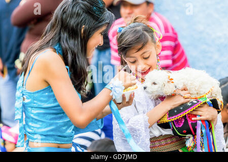 Banos de Agua Santa - 29 novembre : due giovani ragazze vestite di ecuadoriani costumi folk di alimentazione di un cucciolo sulla strada Foto Stock