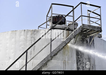 Firefighter getto d'acqua estinguere il fuoco iniziato nei pressi di una benzina serbatoio di stoccaggio Foto Stock