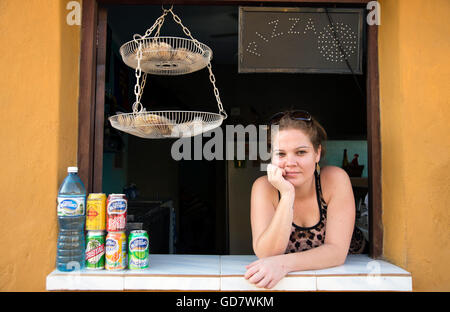 Una giovane donna cubana si appoggia attraverso il portello della sua cucina pizza in Trinidad, Cuba Foto Stock