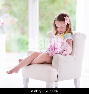 Bambina maleodoranti peonia mazzo di fiori seduto in una sedia bianca nella soleggiata camera da letto. Vivaio interno con i fiori per le ragazze Foto Stock