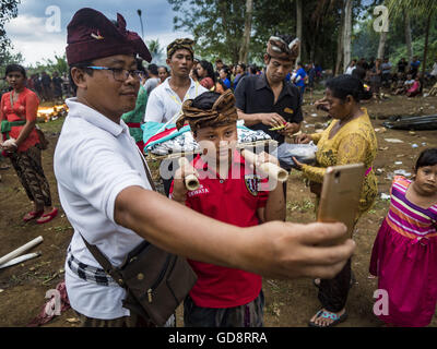 Ubud, Bali, Indonesia. 13 Luglio, 2016. Un padre prende un selfie di suo figlio durante la cremazione di massa in Ubud mercoledì. La popolazione locale in Ubud esumato i resti dei membri della famiglia e bruciò i loro resti in una massa cerimonia di cremazione mercoledì. Quasi un centinaio di persone sarà cremato e sepolto nel più grande di cremazione di massa a Bali negli anni questa settimana. La maggior parte delle persone a Bali sono indù. Cremazioni tradizionale a Bali sono molto costosi, in modo europee detengono solitamente una massa cremazione circa ogni cinque anni. Credito: ZUMA Press, Inc./Alamy Live News Foto Stock