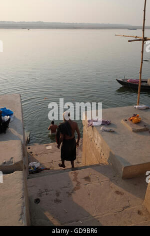Un uomo che fa un passo verso il basso per fare il bagno nel fiume sacro Gange poco dopo l'alba. Varanasi, Uttar Pradesh, India. Foto Stock