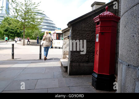 Un iconico red britannico Mail letter box a Londra sul Tamigi la passerella. Municipio di Londra può essere visto in background Foto Stock