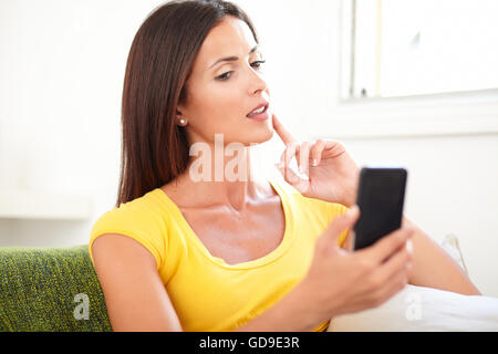 Donna rilassato utilizzando un telefono cellulare mentre si tocca il suo mento con un dito Foto Stock