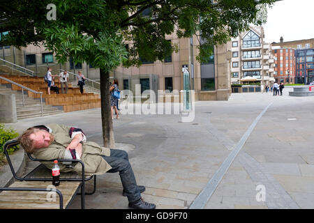 Apparentemente una senzatetto uomo dorme su una panchina di Londra con una bottiglia di Coca Cola sul banco accanto a lui Foto Stock