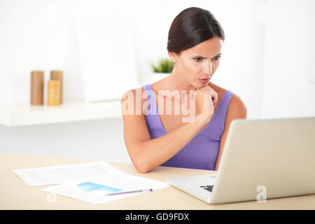 Donna ispanica chiedendo mentre si lavora sul suo computer portatile nella casa di accoglienza Foto Stock