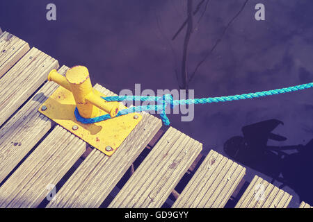 Vintage nei toni del giallo bollard ormeggio con corda blu in marina, quadro concettuale. Foto Stock