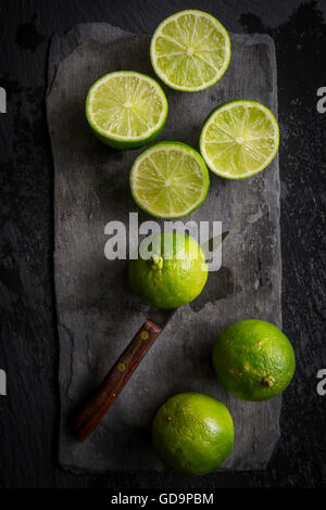 Intero e tagliare limes sul nero ardesia board con l'annata il coltello di taglio del limes. Vista dall'alto. Foto Stock