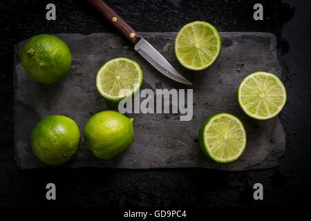 Intero e tagliare limes sul nero ardesia bordo con coltello vintage. Vista dall'alto. Foto Stock