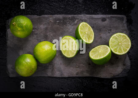 Intero e tagliare limes sul nero ardesia bordo. Vista dall'alto. Foto Stock