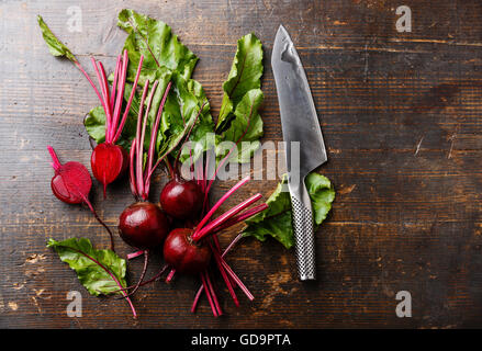 La barbabietola rossa con herbage foglie verdi e coltello da cucina su sfondo di legno Foto Stock