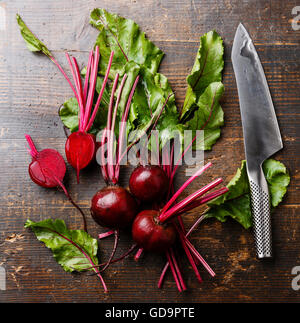 La barbabietola rossa con herbage foglie verdi e coltello da cucina su sfondo di legno Foto Stock