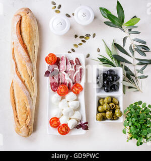 Antipasti sfiziosi snack con verde e balck olive, mozzarella, salsicce, pomodori, erbe fresche e pane su pietra bianca textur Foto Stock