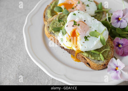 Le uova in camicia con avocado , di germogli di semi di girasole e fiori commestibili sulla pasta madre pane tostato Foto Stock