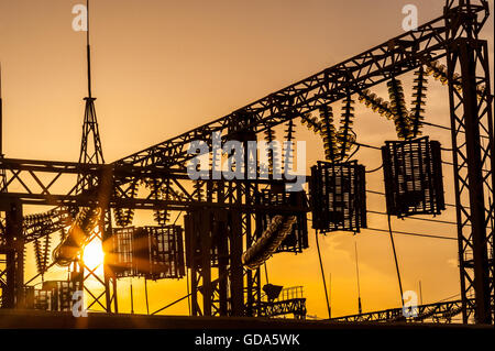 Le linee elettriche, i poli e gli isolatori di vetro in una stazione di alimentazione al tramonto Foto Stock